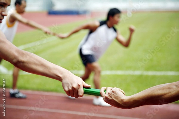 Fototapeta Man passing baton to his teammate in a relay event