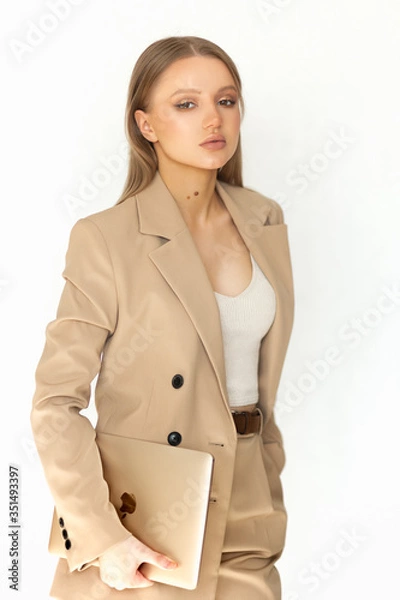 Obraz Beautiful woman businesswoman in a beige suit holds a laptop in her hand and looks at the camera. Isolated on a white background. A great example of office wear.