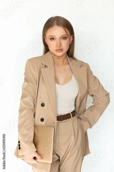 Obraz Beautiful woman businesswoman in a beige suit holds a laptop in her hand and looks at the camera. Isolated on a white background. A great example of office wear.