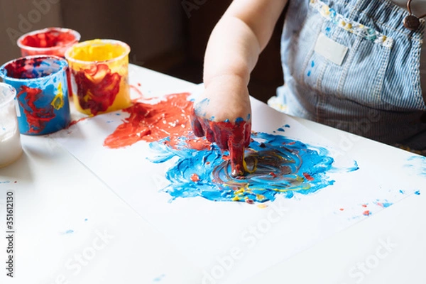 Fototapeta Child painting with her hands on the table at home using blue and red paint. Finger painting or art therapy for children. Fun activities for toddlers. Close up.  