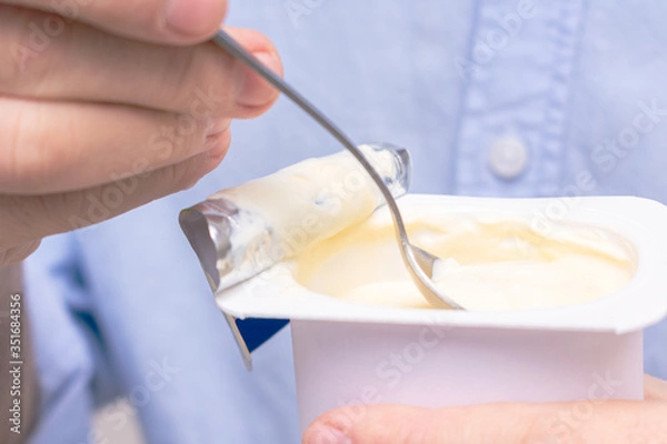 Obraz Person holding yogurt while eating, man's hand, close up, cropped image