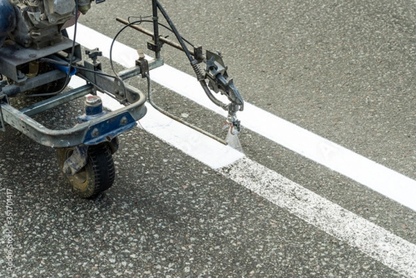 Fototapeta Automated painting by airbrushing of a road using spraying for driving direction, road repair marking on asphalt pavement