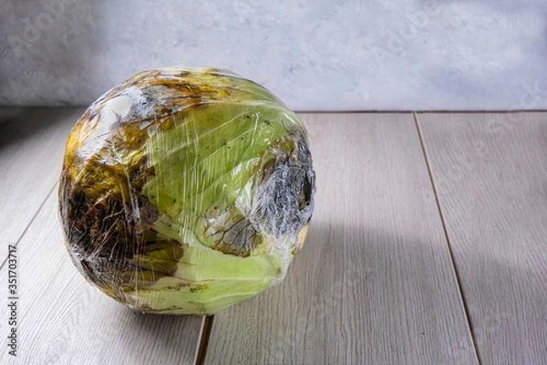 Fototapeta The cabbage is wrapped in cellophane. A spoiled vegetable. The concept of Ugly products, no plastic packaging. Copy space