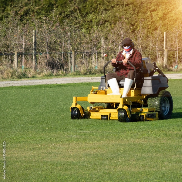 Fototapeta Soft focus of Gardener use Lawn mover on green grass in the modern garden, Machine for cutting lawns, the orange sunlight splashes behind and the green background fence, mow the lawn service concept.
