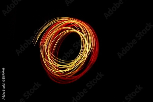 Fototapeta Long exposure photograph of neon red and gold colour in an abstract swirl, parallel lines pattern against a black background. Light painting photography.