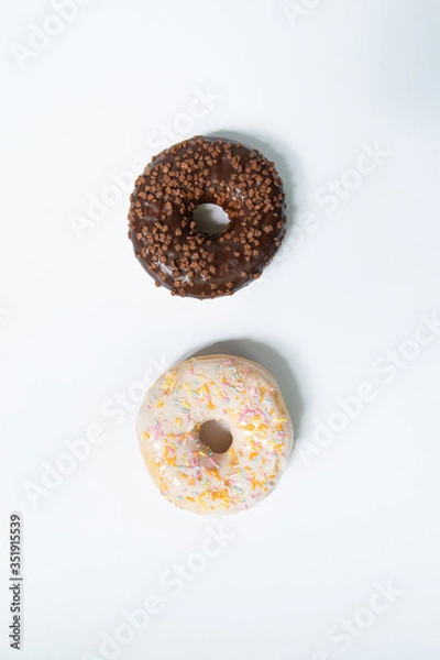 Fototapeta Donut day. Two bright colored donuts with colorful sprinkles on white background. Copy space, close-up