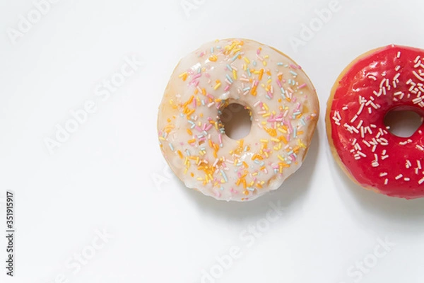Fototapeta Donut day. Two bright colored donuts with colorful sprinkles on white background. Copy space, close-up