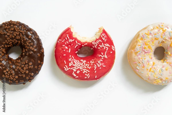 Fototapeta Donut day. Bitten colored donuts with colorful sprinkles on white background. Copy space, close-up