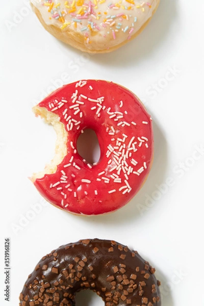 Fototapeta Donut day. Bitten colored donuts with colorful sprinkles on white background. Copy space, close-up