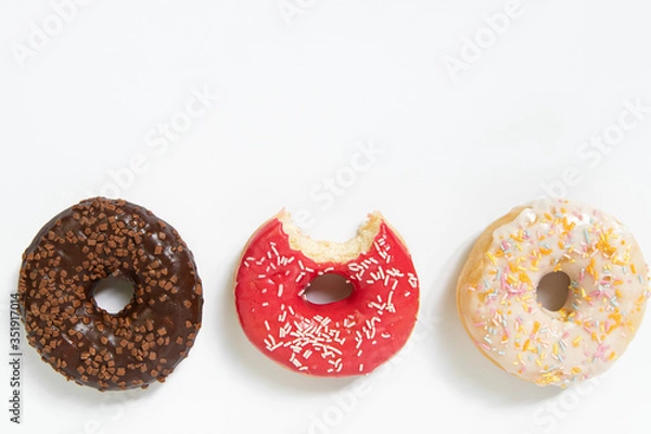 Fototapeta Donut day. Bitten colored donuts with colorful sprinkles on white background. Copy space, close-up
