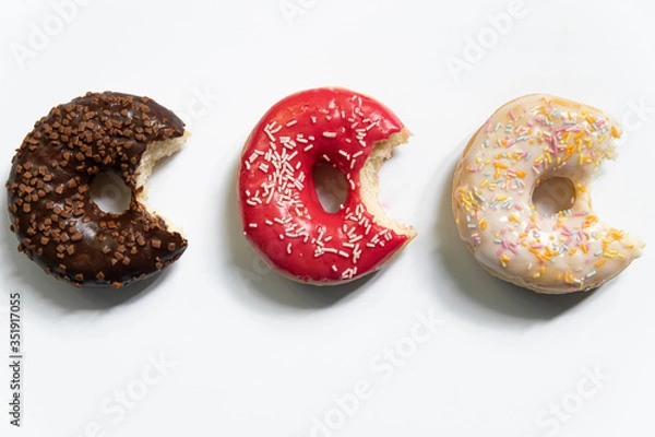 Fototapeta Donut day. Bitten colored donuts with colorful sprinkles on white background. Copy space, close-up