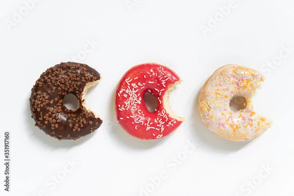 Fototapeta Donut day. Bitten colored donuts with colorful sprinkles on white background. Copy space, close-up
