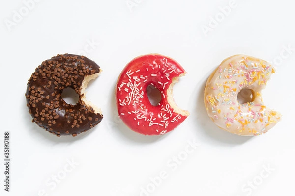 Fototapeta Donut day. Bitten colored donuts with colorful sprinkles on white background. Copy space, close-up