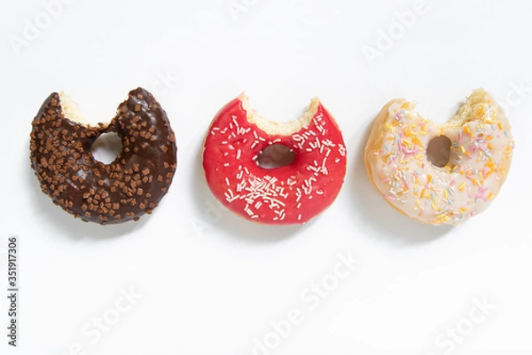 Fototapeta Donut day. Bitten colored donuts with colorful sprinkles on white background. Copy space, close-up