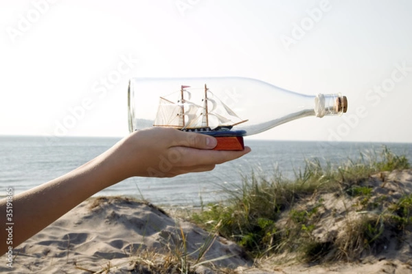 Fototapeta Man is holding miniature ship in bottle