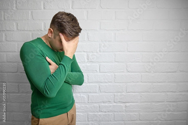 Fototapeta Portrait of young man with face palm gesture. Disappointed stressed out male making facepalm with hand. Brick wall background. Studio photo. There is a place to copy space.
