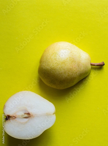 Fototapeta Yellow fresh pear cut in half on yellow background. Top view.