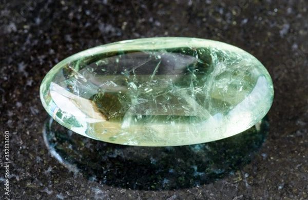 Fototapeta closeup of sample of natural mineral from geological collection - tumbled Prasiolite (green quartz) rock on black granite background from Brazil