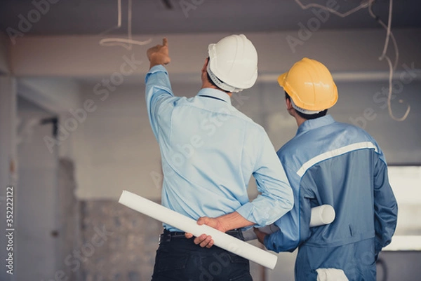 Fototapeta Engineer team with hard hat and blueprint talking together at the building construction site.