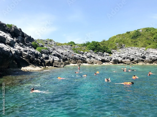 Fototapeta People in the sea, swim and dive around the cliff.
