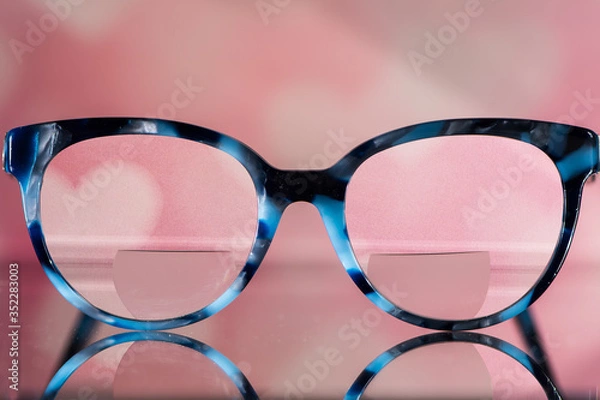 Obraz Eyeglasses Glasses with Bifocals and Black and blue Frame smudged view agaist a blurry pink  background with white hearts. Blurry Vision Concept