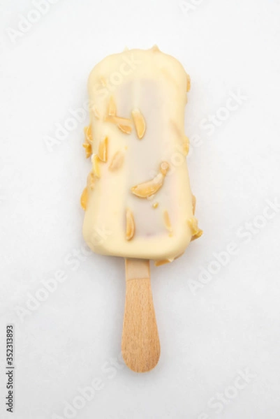 Fototapeta ice cream on a wooden stick in white chocolate glaze with nuts on a white background