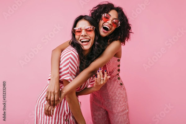 Fototapeta African sisters with dark curls are having fun in wonderful mood. Portrait of embracing girls with beautiful appearance