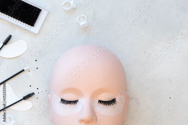 Fototapeta A beauty background with eyelash extension theme.  A mannequin training head with strip lashes is set out in the lower part of the image.  Space for copy on a plain white background.