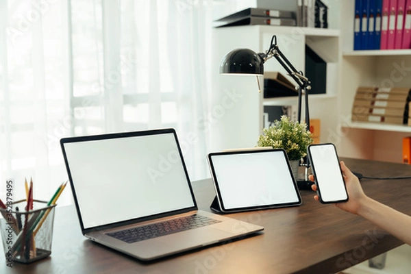Fototapeta Woman using digital laptop and tablet with smartphone on the table in house. Blank screen for advertising.