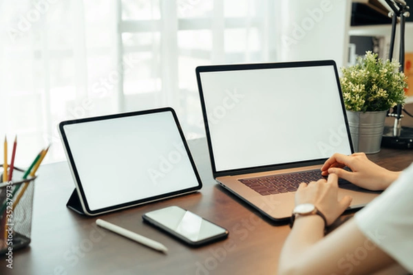 Fototapeta Woman using digital laptop and tablet with smartphone on the table in house. Blank screen for advertising.