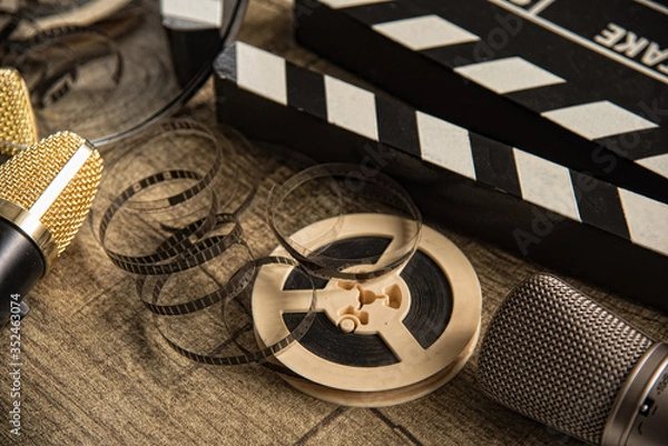 Fototapeta Film reel, movie clapperboard and two microphones on a table with