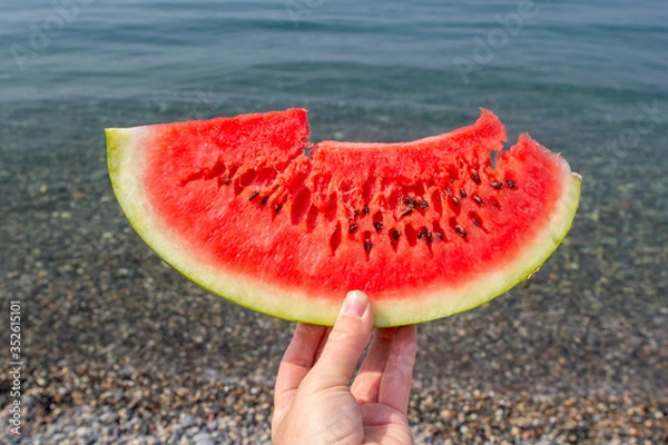 Fototapeta Juicy watermelon in hand on the background of the sea. Hand holding piece of watermelon on the background of sea.