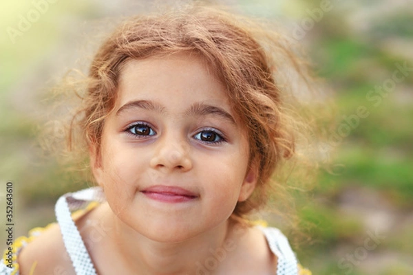 Obraz Portrait of smiling cute little girl at green of summer park. Happy child looking at the camera