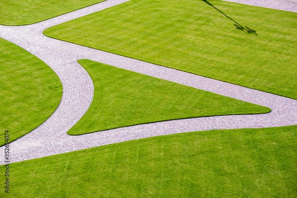 Obraz Cobbled park alleys surrounded by green grass on a sunny, bright spring day. Lamp shade visible on grass. Park seen from above.