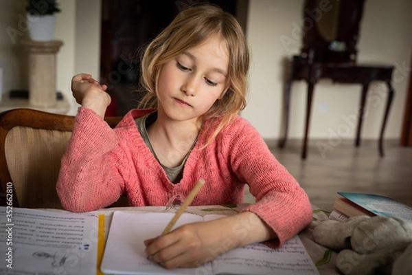 Obraz blond lefthanded girl writting homeworks during corona virus lockdown restrictions