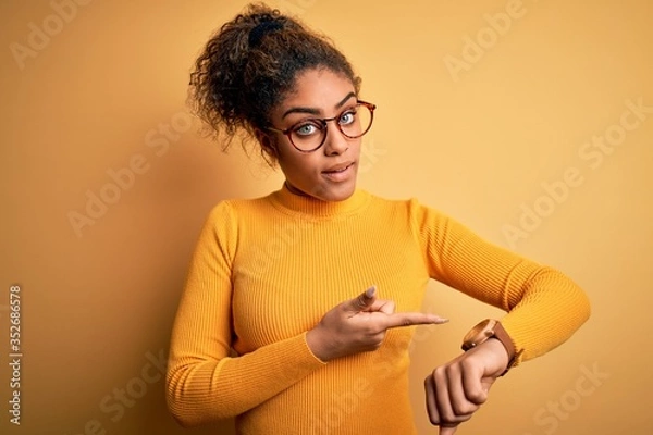 Fototapeta Young beautiful african american girl wearing sweater and glasses over yellow background In hurry pointing to watch time, impatience, upset and angry for deadline delay