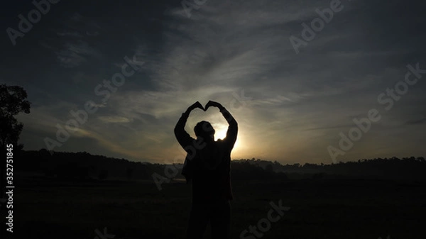 Obraz A woman standing facing the sun Looking at a wide field, heart-shaped arms, sun light shining through the model.