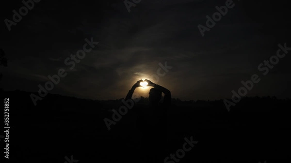 Obraz A woman standing facing the sun Looking at the wide field, heart-shaped hand-made, the light of the sun shining through the model.