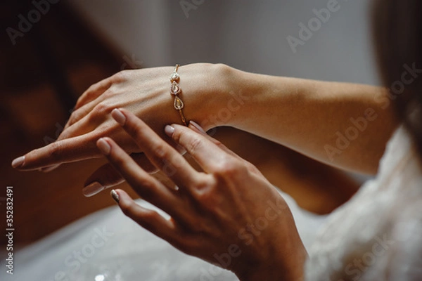 Obraz Beautiful elegant bride puts a bracelet on her hand, closeup. Girl put a bracelet on arm.Preparing the bride for the wedding ceremony.