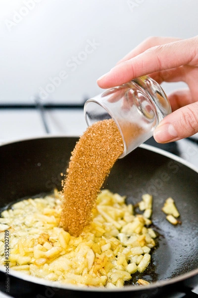 Fototapeta Someone´s hand adding the brown sugar to he pan with chopped apple