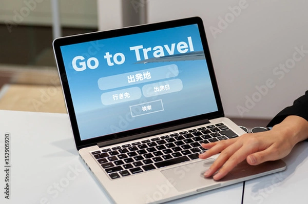 Fototapeta GO TO TRAVEL キャンペーン　　Go Toキャンペーン
旅行のオンライン予約検索のイメージ　ノートパソコンで旅行の予約検索の画面を見せている女性の手