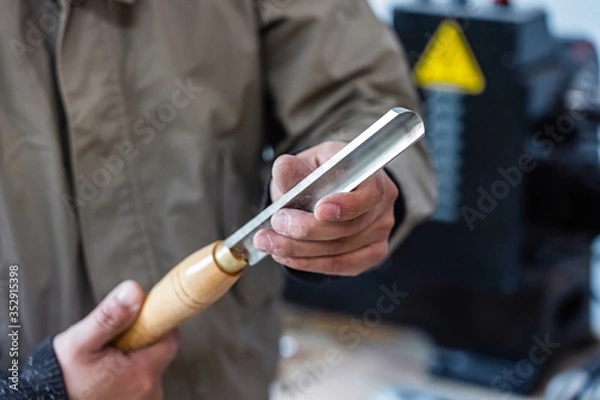 Fototapeta Man is holding the chisel for woodwork. Worker is keeping the new metal tool at workshop.