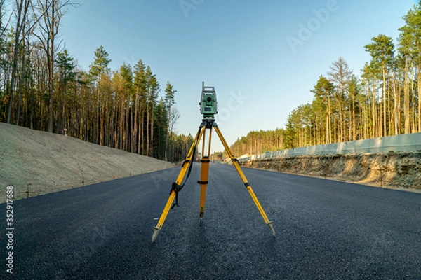 Fototapeta Surveyors equipment (theodolite or total positioning station) on the construction site of the road or building with construction machinery background