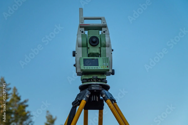 Fototapeta Surveyors equipment (theodolite or total positioning station) on the construction site of the road or building with construction machinery background
