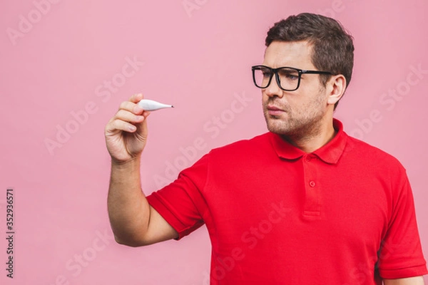 Fototapeta Virus concept. Young caucasian man holding a thermometer isolated over pink background.