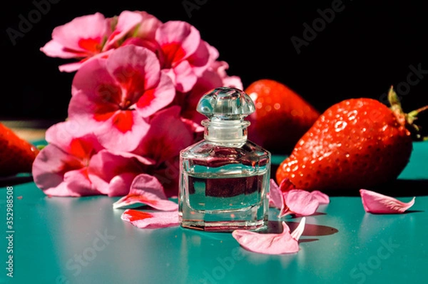 Fototapeta Beautiful contrast composition with elegant small perfume bottle, pink flower and strawberries on the dark background. Selective focus.