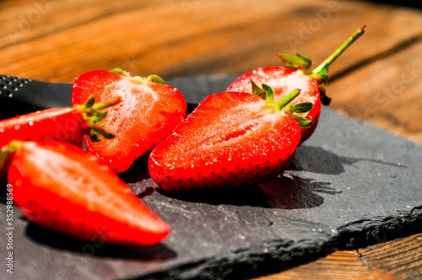 Fototapeta Juicy red freshly cut in half strawberries on a stone texture background. Close up sunlit half of strawberries.