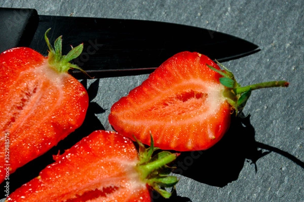 Fototapeta Juicy red freshly cut in half strawberries on a stone texture background. Close up sunlit half of strawberries.