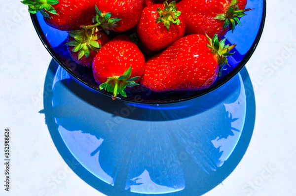 Fototapeta Delicious red ripe strawberries in a blue vase on the white background. Beautiful art shadows of berries in a bowl.