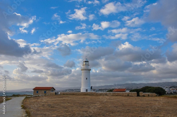 Fototapeta Solitary, white, beautiful lighthouse standing in the wild field under the scenic cloudy sky.